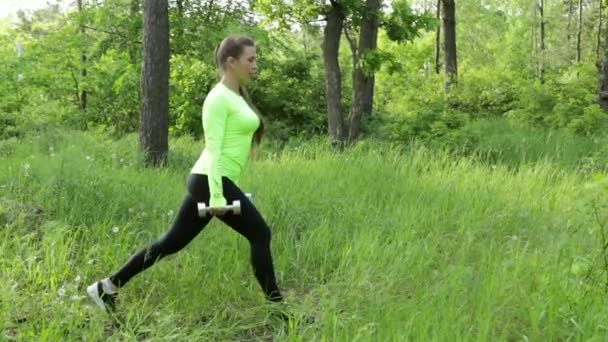 Mujer joven haciendo ejercicio haciendo agacharse con dumbbels en el parque — Vídeo de stock