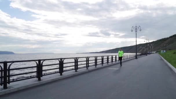 Caucasian brunette woman in sports cloth runs on embankment near the river — Stock Video