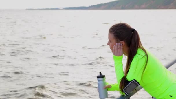 Deporte mujer mirada mar tomar un descanso beber agua en la ciudad terraplén — Vídeos de Stock