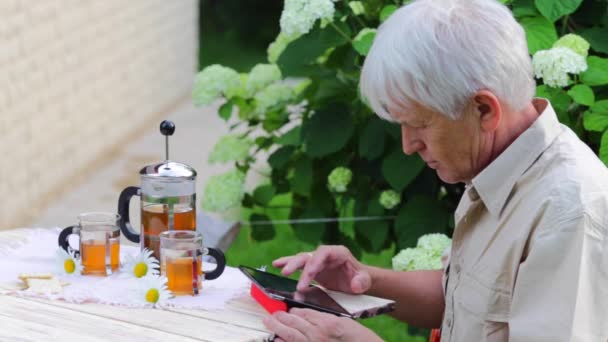 Hombre elemental usando tableta digital en mesa de jardín de verano con té — Vídeos de Stock