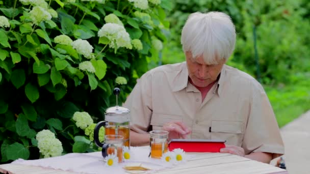 Hombre mayor usando tableta digital en mesa de jardín de verano con té — Vídeos de Stock