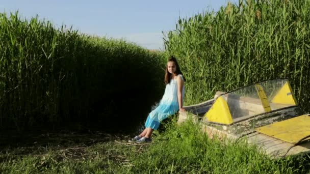 Dospívající dívka sedící na staré lodi poblíž jezera venkovských zelené rákosí pozadí — Stock video