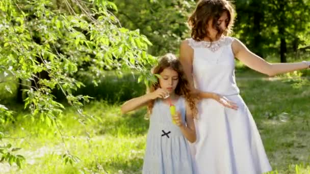 Beautiful young mother together with her daughter in nature making soap bubbles — Stock Video