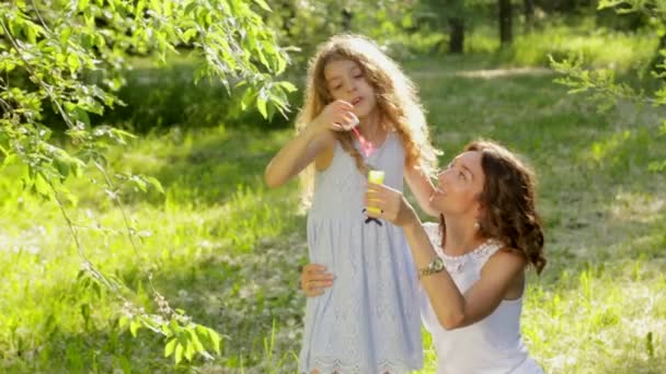 Beautiful young mother together with her daughter in nature making soap bubbles — Stock Video