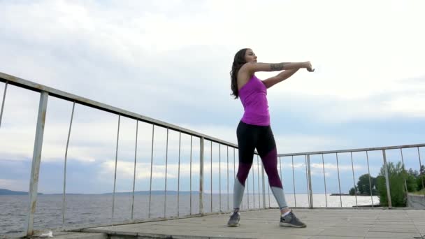 Una ragazza in forma sull'argine del fiume. Esercizi di pratica. Rallentatore . — Video Stock