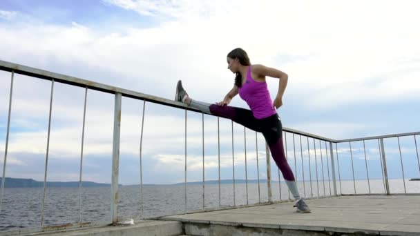 Fitness girl on the embankment of the river. Practice exercises on the railing. — Stock Video