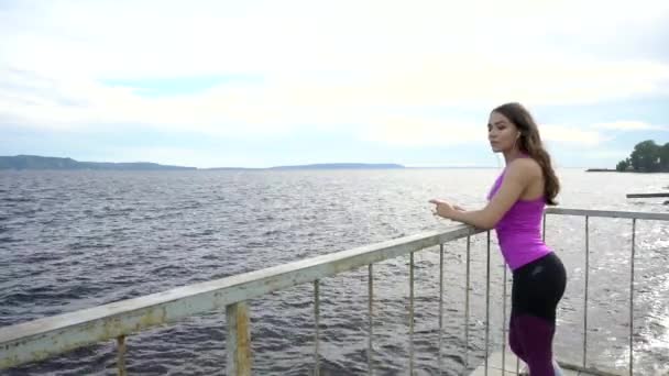 Fitness dívka na nábřeží řeky. Odpočiňte si při poslechu hudby 4k — Stock video