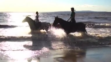 Su günbatımı ışıkta at nehir Plajı'nda iki kadın binmek