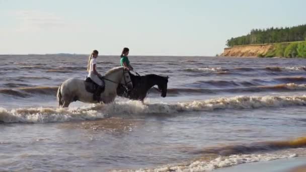 Two women ride on horse at river beach in water sunset light — Stock Video