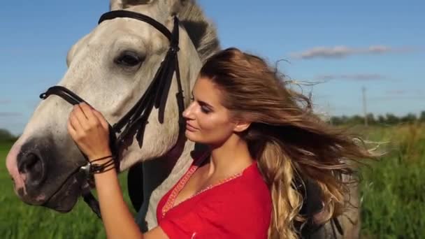 Portrait de jeune belle femme dreesed en rouge avec cheval blanc près du champ — Video