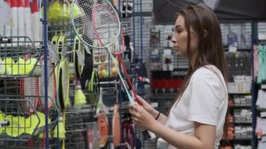 Kadın alışverişçi spor malzemeleri mağazasından badminton raketleri seçiyor.
