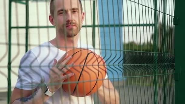 Uomo sportivo con palla arancione al campo da basket aperto, ritratto — Video Stock