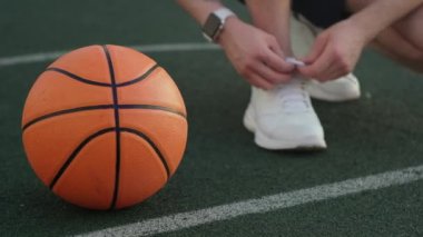 Spor ayakkabıları bağlayan, basketbol topunun yanında poz veren meçhul sporcu.