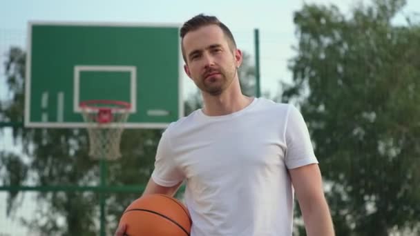 Ragazzo che tiene una palla mentre posa al campo da basket — Video Stock
