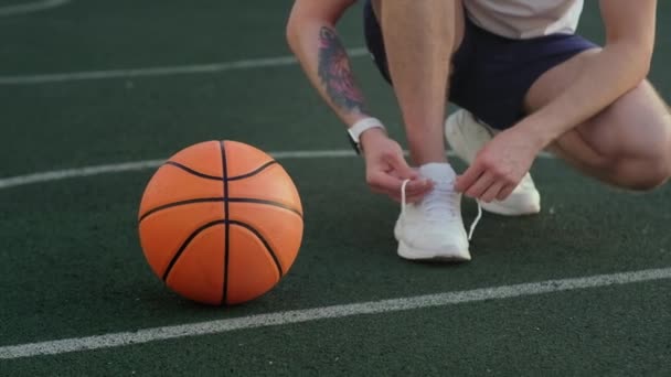 Basketball player is tying lace on sporty shoes on court — Stock Video