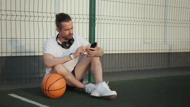 Man santai setelah latihan basket dan mencari musik di smartphone — Stok Video