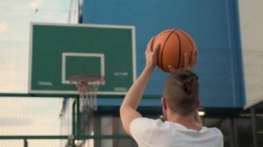 Tanınmayan genç adam dışarıda basketbol oynuyor.