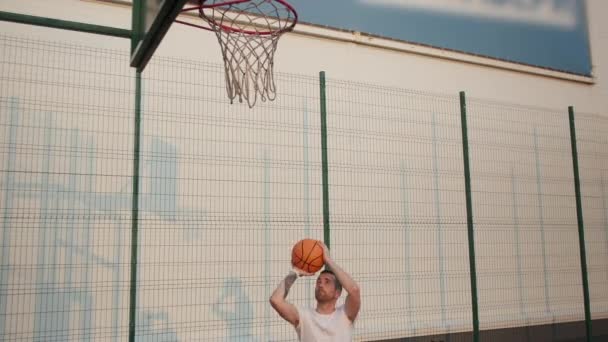 Молодий чоловік робить цілі, граючи в баскетбол на вулиці — стокове відео
