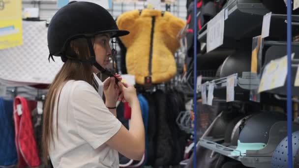 Девушка покупает шлем для верховой езды в спортивном магазине — стоковое видео