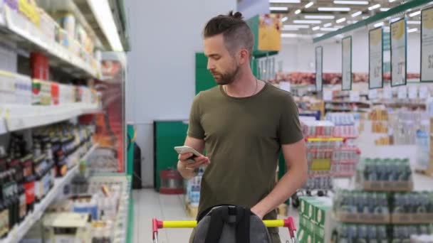 젊은 남성이 슈퍼마켓에서 맥주를 고르면서 휴대 전화를 사용하고 있다 — 비디오
