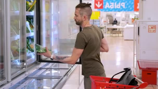 Jeune homme achetant des légumes surgelés en magasin — Video