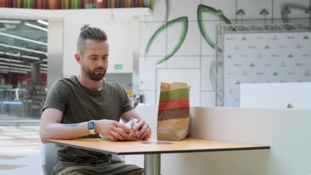 Man är på väg att njuta av hamburgare sitter vid bordet i café på stormarknad — Stockvideo