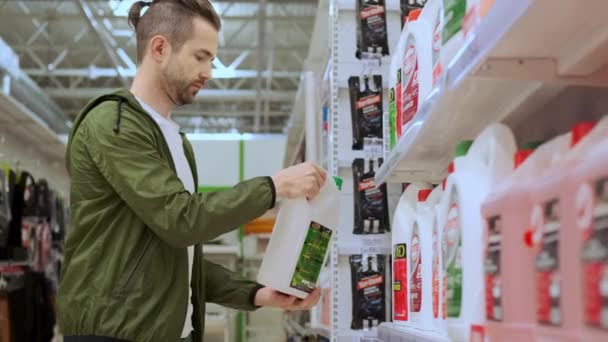 Junger Mann kauft Frostschutzmittel oder Kühlmittel in Spezialgeschäft — Stockvideo