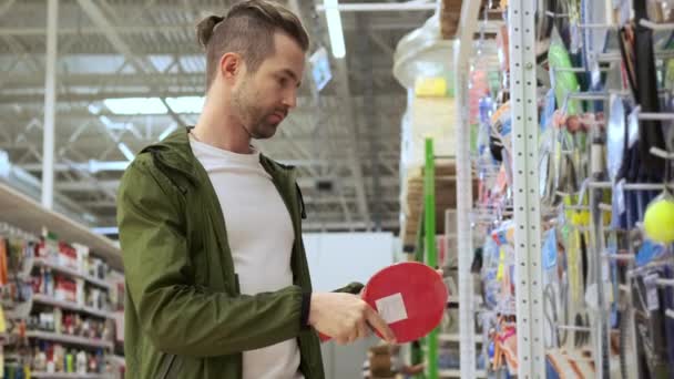 Jeune homme achète une raquette de tennis de table dans un magasin de sport — Video