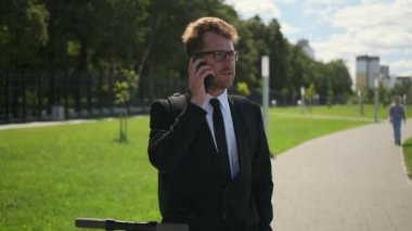 Açık havada akıllı telefondan konuşan bir iş adamı, yakınlarda elektrikli scooter.