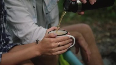 Orman kampı, turistler çay içiyor, erkekler kadınlar için sıcak içecek koyuyor.