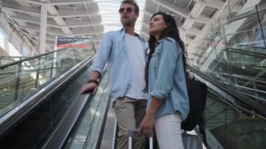 İstasyonda bavullu tren yolcuları yürüyen merdivende.