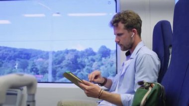 Adam trenle seyahat ediyor, tabletteki resimlere bakıyor.