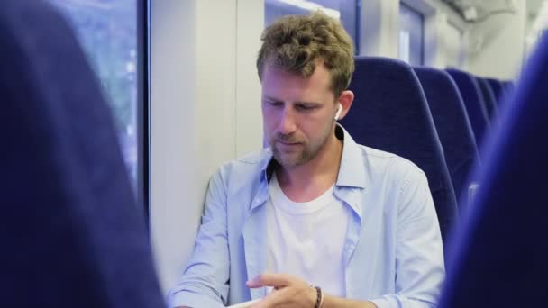 Młody mężczyzna w słuchawkach bezprzewodowych podczas podróży pociągiem — Wideo stockowe
