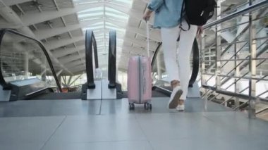 Sırt çantalı genç bayan tren istasyonunda yürüyen merdivene biniyor.