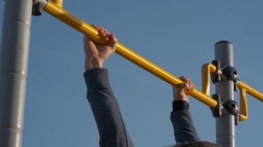Erkek sporcu dışarıda yatay bar egzersizi yapıyor.