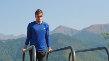 Sporcu açık alanda spor ekipmanları üzerinde şınav çekiyor.