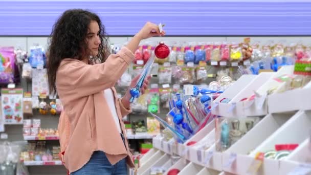 Vrouwelijke klant kiest glanzende kerstversiering voor boom en interieur van appartement in supermarkt — Stockvideo