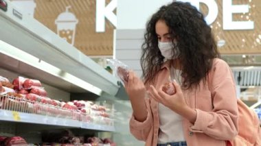 Yüzü maskeli kadın müşteri markette sosis seçiyor.