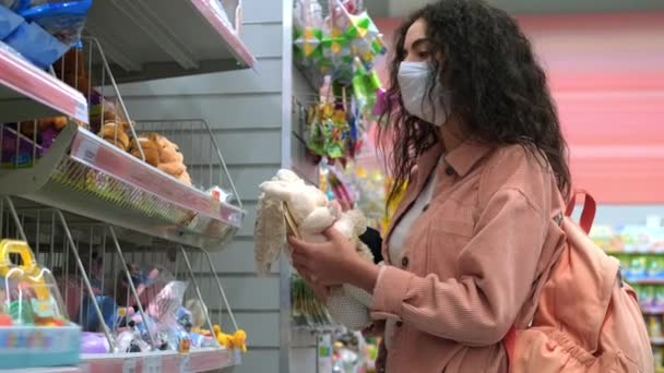 Compras en pandemia, mujer con mascarilla está eligiendo juguetes en la tienda de niños — Vídeos de Stock