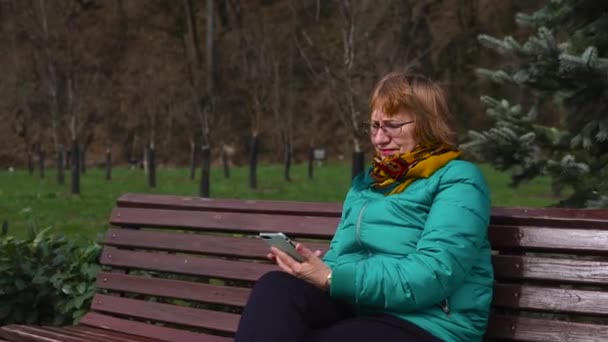 Femeie în vârstă cu mobilă așezată pe bancă afară — Videoclip de stoc