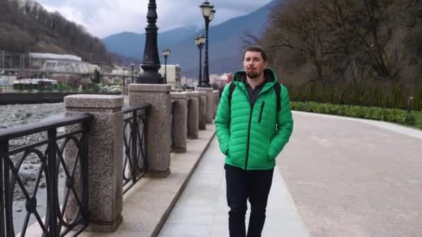 Male tourist is strolling along city embankment of river at autumn day — Stock Video