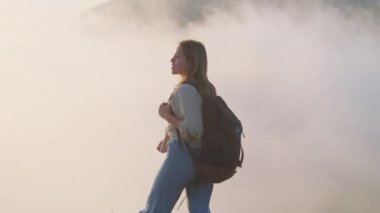 Turist kız bulutların içinde dağın tepesinde yürüyor.