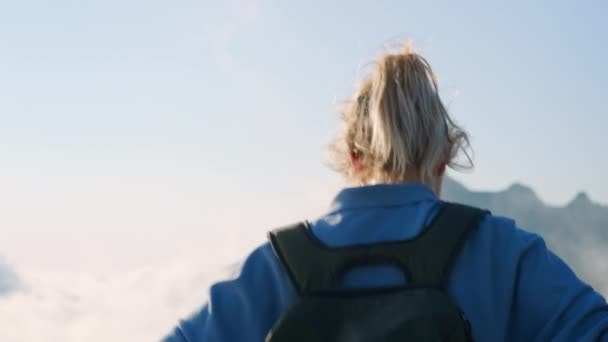 Vrouwelijke wandelaar loopt op de top van de berg boven wolken — Stockvideo