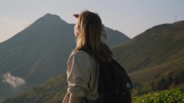 Sırt çantalı kadın dağın tepesinde duruyor ve doğaya hayran.