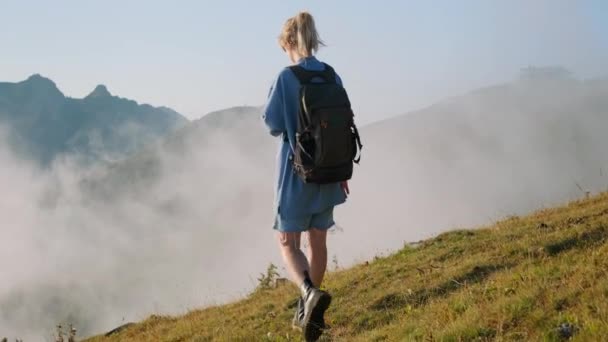 Zorgeloze jonge vrouw loopt alleen op de top van de berg boven wolken, achteraanzicht — Stockvideo