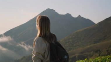 Genç kadın dağın ya da tepenin tepesinde duruyor ve manzaraya hayran.