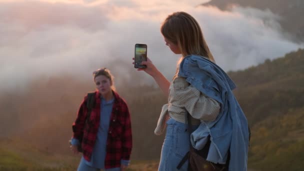 Teen girl sta scattando foto da smartphone della sua amica sulla cima della montagna al tramonto — Video Stock