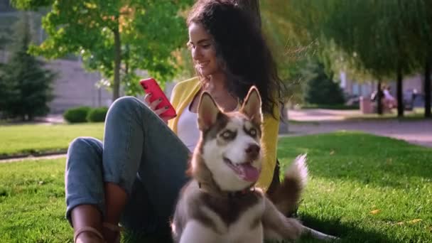 Ung kvinde og hendes hund hviler sammen i parken om sommeren – Stock-video