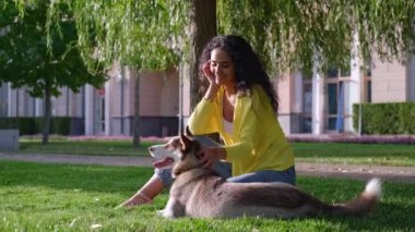 Parkta köpek, genç kadın ve evcil hayvanı yeşil çimlerin üzerinde oturuyorlar.