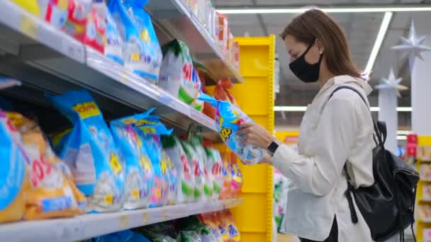Молодая домохозяйка в маске выбирает стиральный порошок в супермаркете — стоковое видео